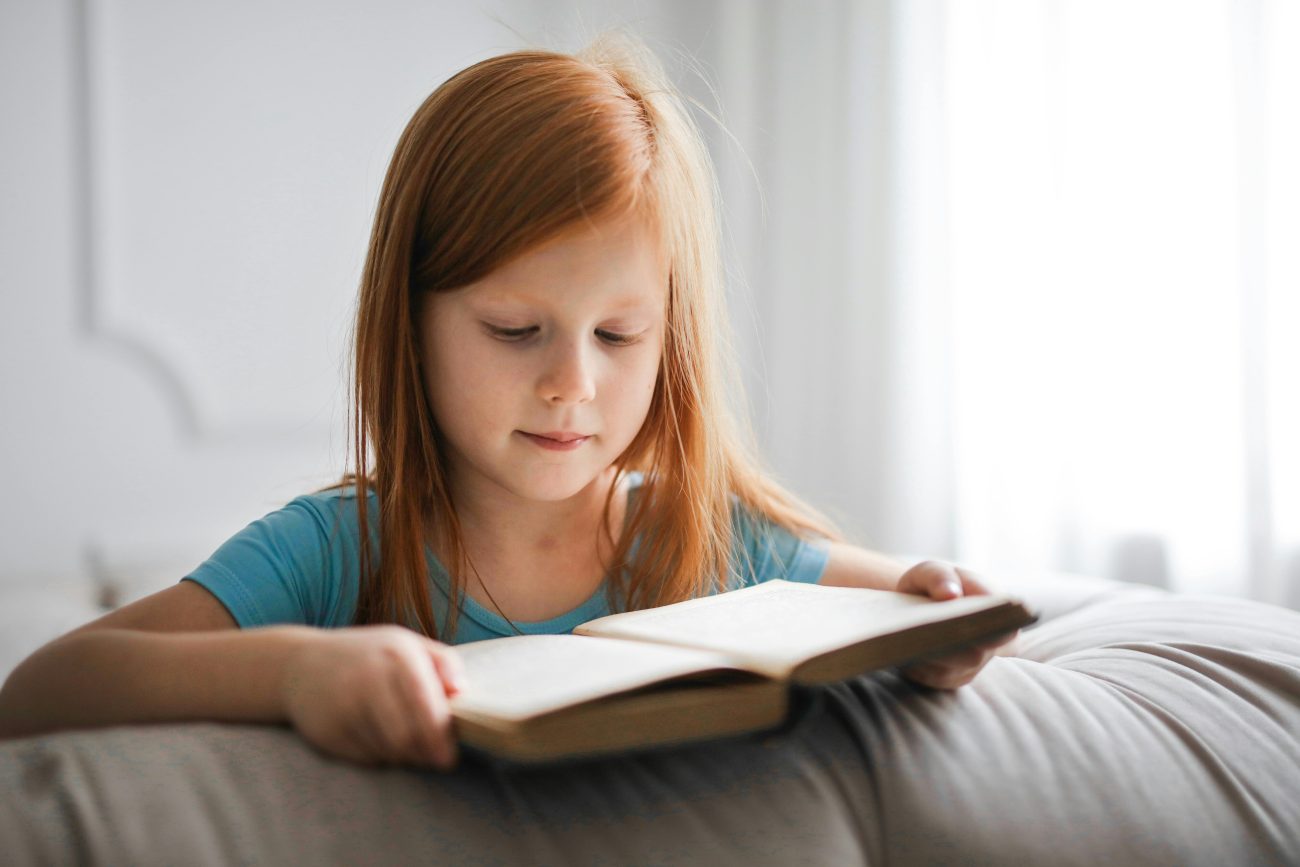 A primary school aged redhead girl reading a book.